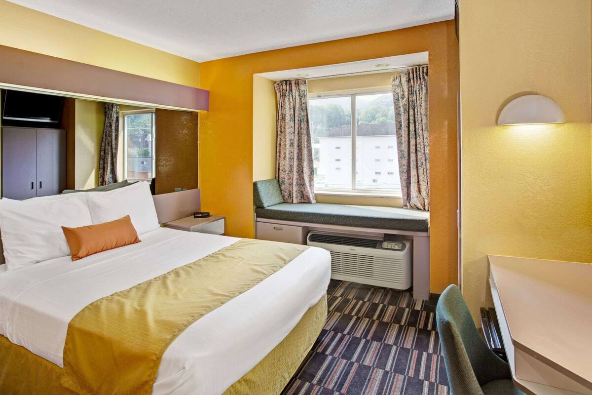 Habitación de hotel con cama, escritorio, silla, ventana con cortinas y calefactor.