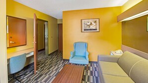 Habitación de hotel con un sillón azul, un sofá, una mesa de centro de madera y un cuadro enmarcado en la pared.