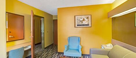 Habitación de hotel con un sillón azul, un sofá, una mesa de centro de madera y un cuadro enmarcado en la pared.
