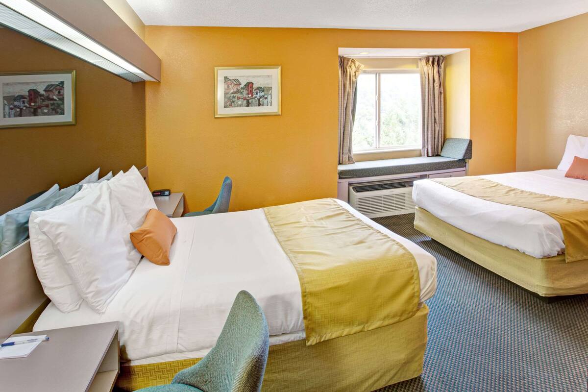Habitación de hotel con dos camas, un escritorio y una ventana con cortinas.