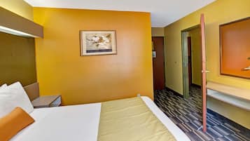Habitación de hotel con cama, escritorio, silla, un cuadro en la pared y una puerta que da a otra habitación.