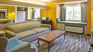 Habitación de hotel con sofá, una mesita, microondas, escritorio, silla, ventana con cortinas y espejo.