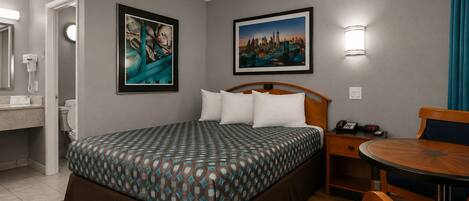 A hotel room with a bed, bedside table, chair, and a view of a cityscape.