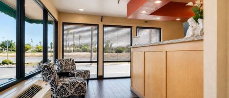 A reception area with a reception desk, two patterned chairs, a large window with blinds, and a view of the outside.