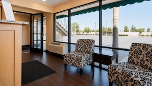 A hotel lobby with a reception desk, a staircase, and two patterned armchairs. - Vagabond Inn Bakersfield South (Bakersfield)