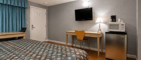 A hotel room with a bed, a desk, a chair, a television, a lamp, and a refrigerator.