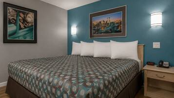 A hotel room with a bed, two wall-mounted light fixtures, a framed picture, a bedside table with a phone, and a clock.