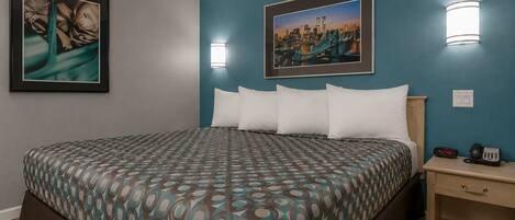 A hotel room with a bed, two wall-mounted light fixtures, a framed picture, a bedside table with a phone, and a clock.