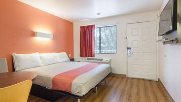 Une chambre d’hôtel avec un lit, un bureau, une télévision et une fenêtre avec des rideaux.