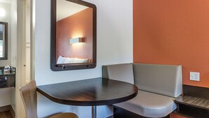 A small, modern room with a round table, two chairs, a bench, a mirror, and a wall-mounted light fixture. - Motel 6 Fresno, CA (Fresno)