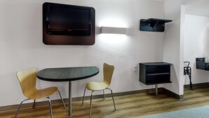 A modern room with a flat-screen TV mounted on the wall, a round table, two chairs, and a black storage unit. - Motel 6 Fresno, CA (Fresno)