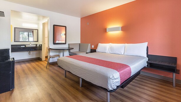 A hotel room with a bed, a desk, a chair, and a small table. - Motel 6 Fresno, CA (Fresno)