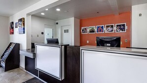 A reception area with a counter, a digital screen, and a wall with framed photos. - Motel 6 Fresno, CA (Fresno)
