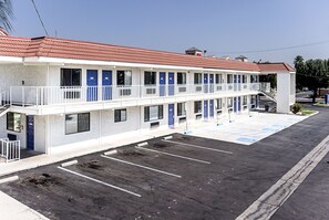 A motel with a two-story structure, multiple rooms with blue doors, a parking lot, and a red-tiled roof. - Motel 6 Fresno, CA (Fresno)