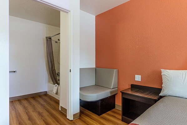 Una habitación pequeña con ducha, un banco, una cama y una mesita.