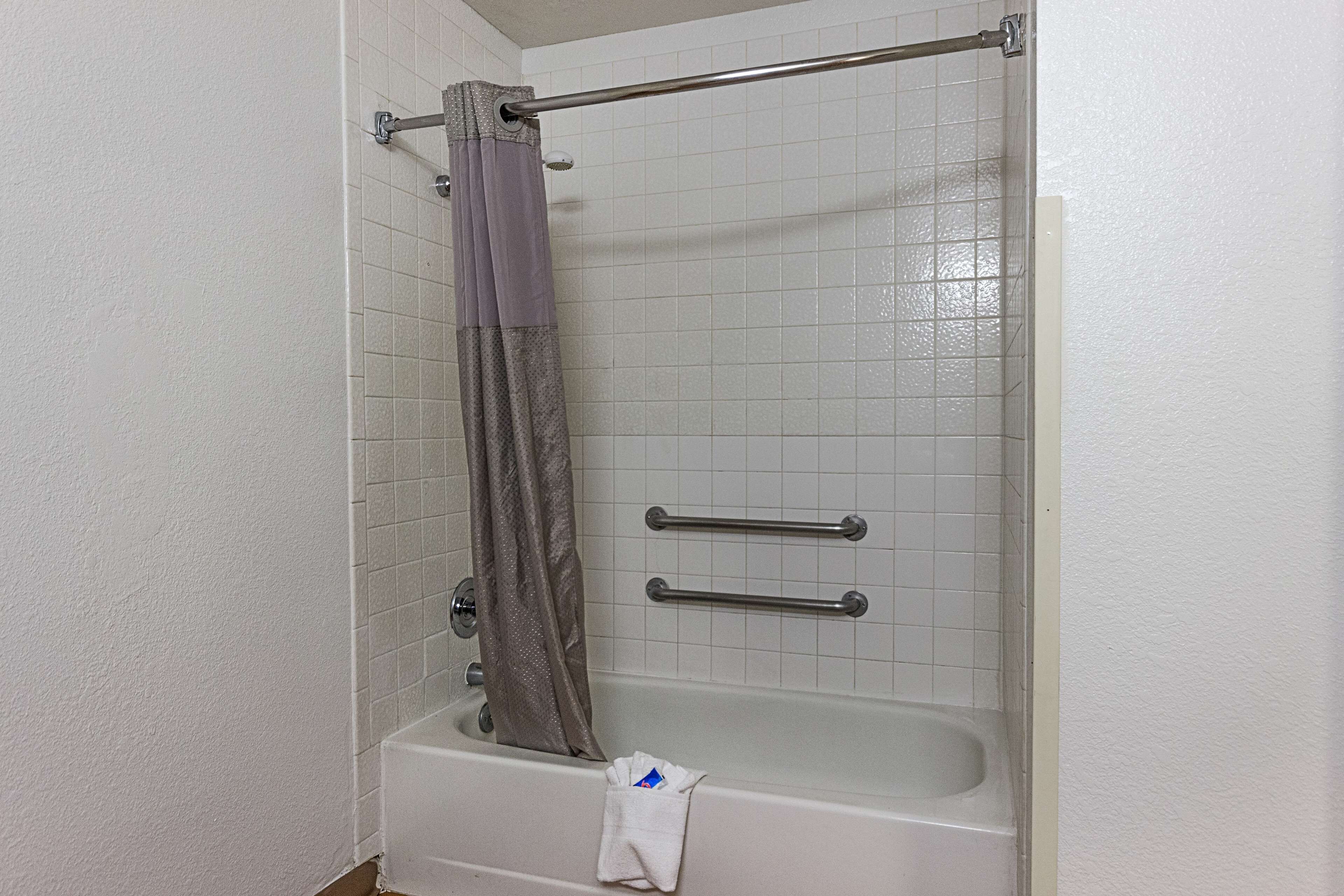 A bathroom with a bathtub, a shower curtain, and two grab bars.