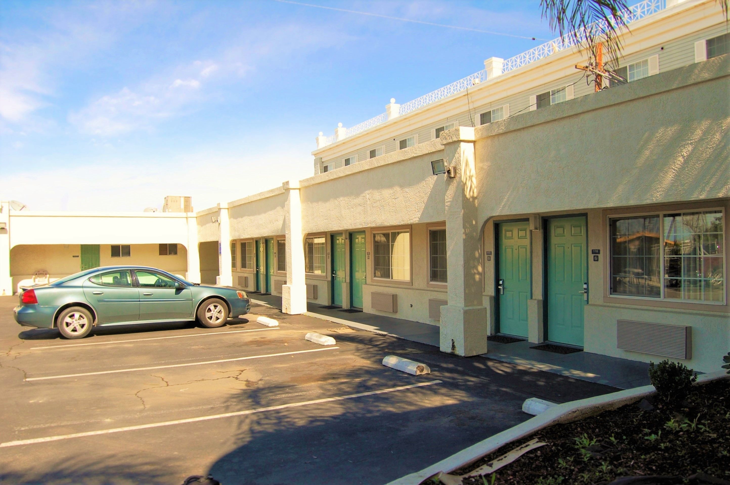 A row of motel rooms with individual doors and windows, a parking lot, and a car parked in front.