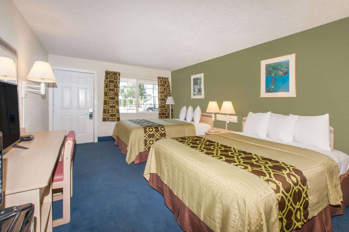 A hotel room with two beds, a desk, a chair, and a TV.
