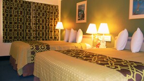 A hotel room with two beds, patterned bedspreads, two bedside lamps, and a patterned curtain.