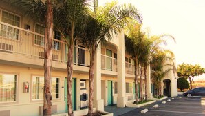 A multi-story hotel with balconies, palm trees, and a parking lot.