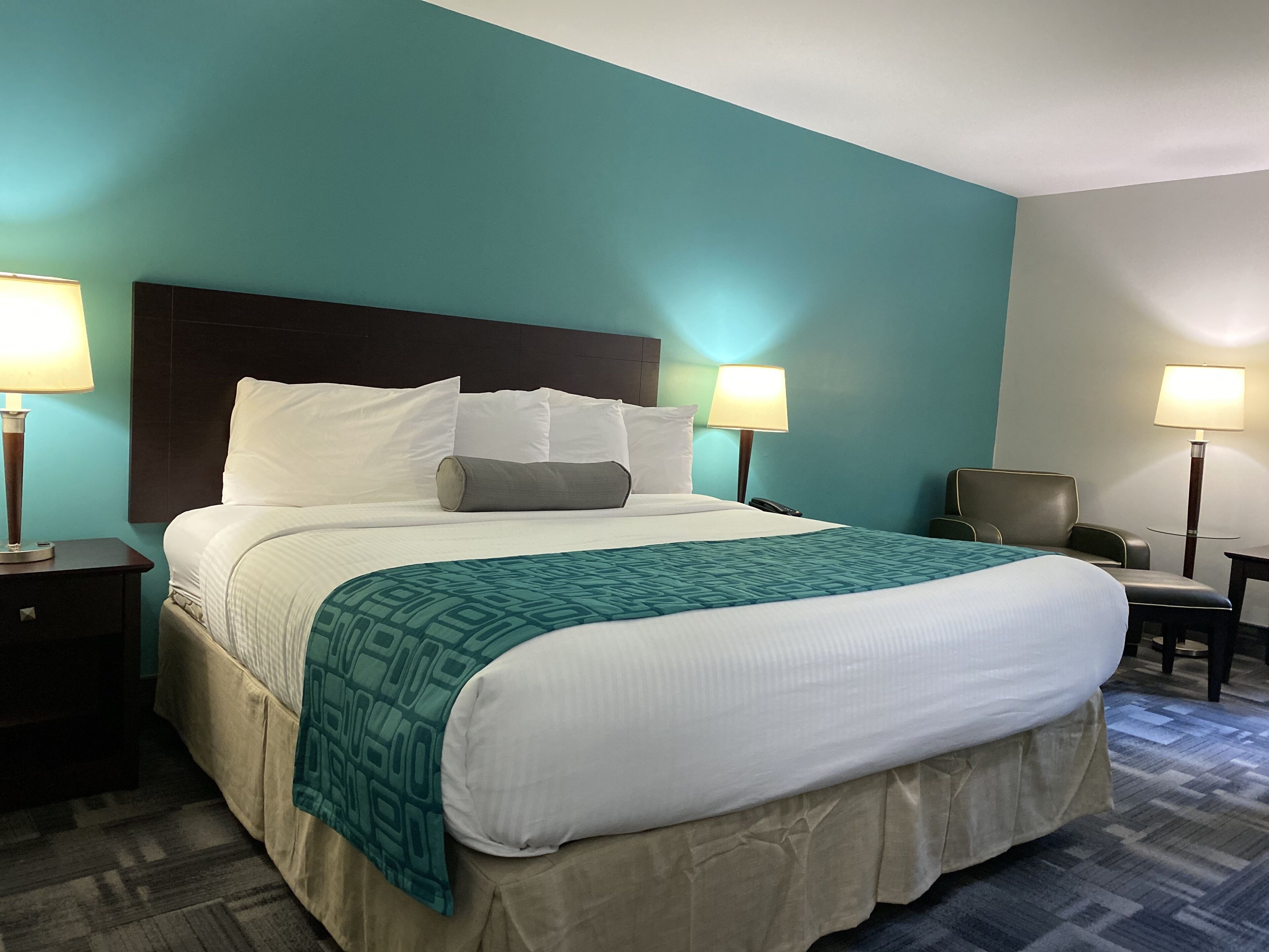 A hotel room with a large bed, two bedside lamps, a chair, and a desk.