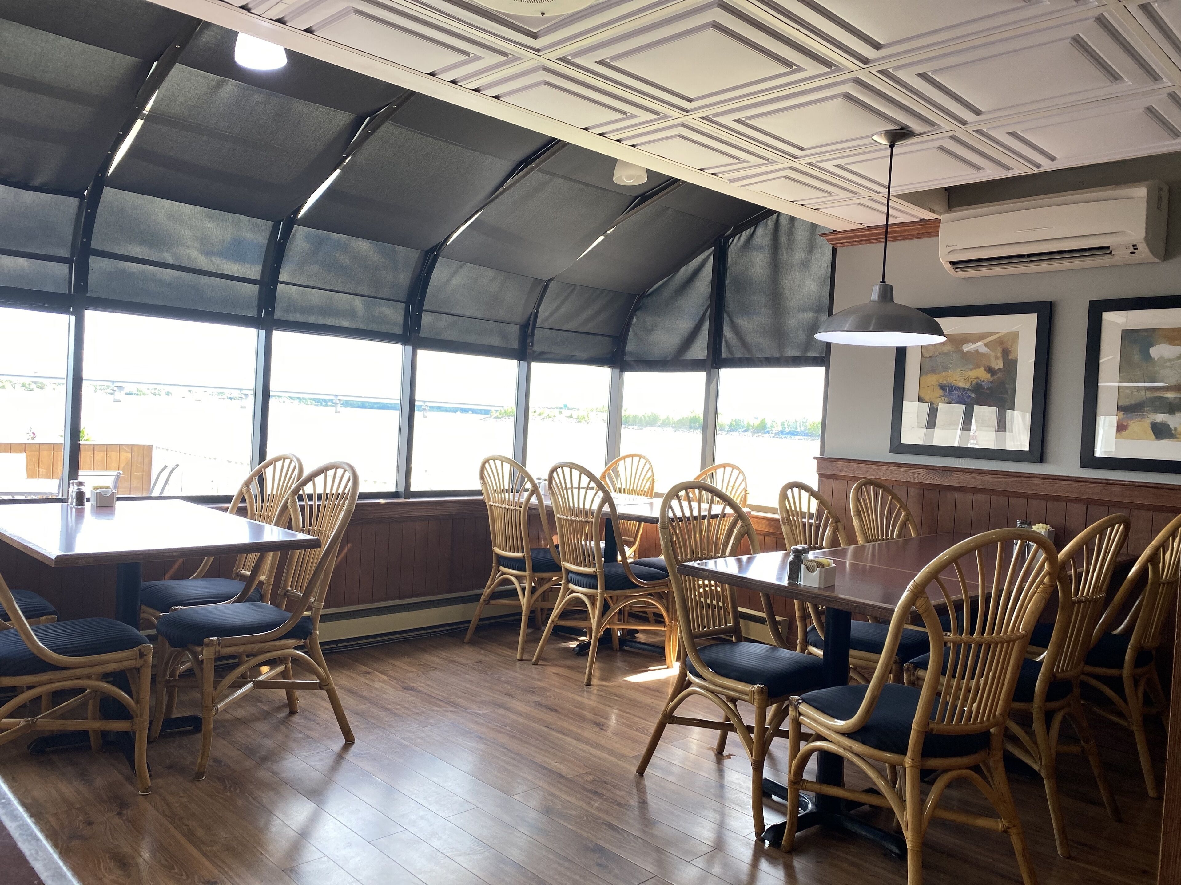 A restaurant with wooden flooring, wicker chairs, and a large window overlooking a body of water.