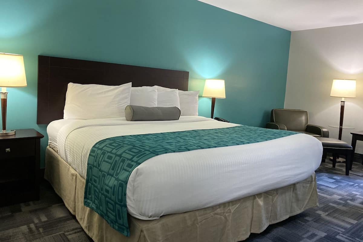 A hotel room with a large bed, two bedside lamps, a chair, and a desk.