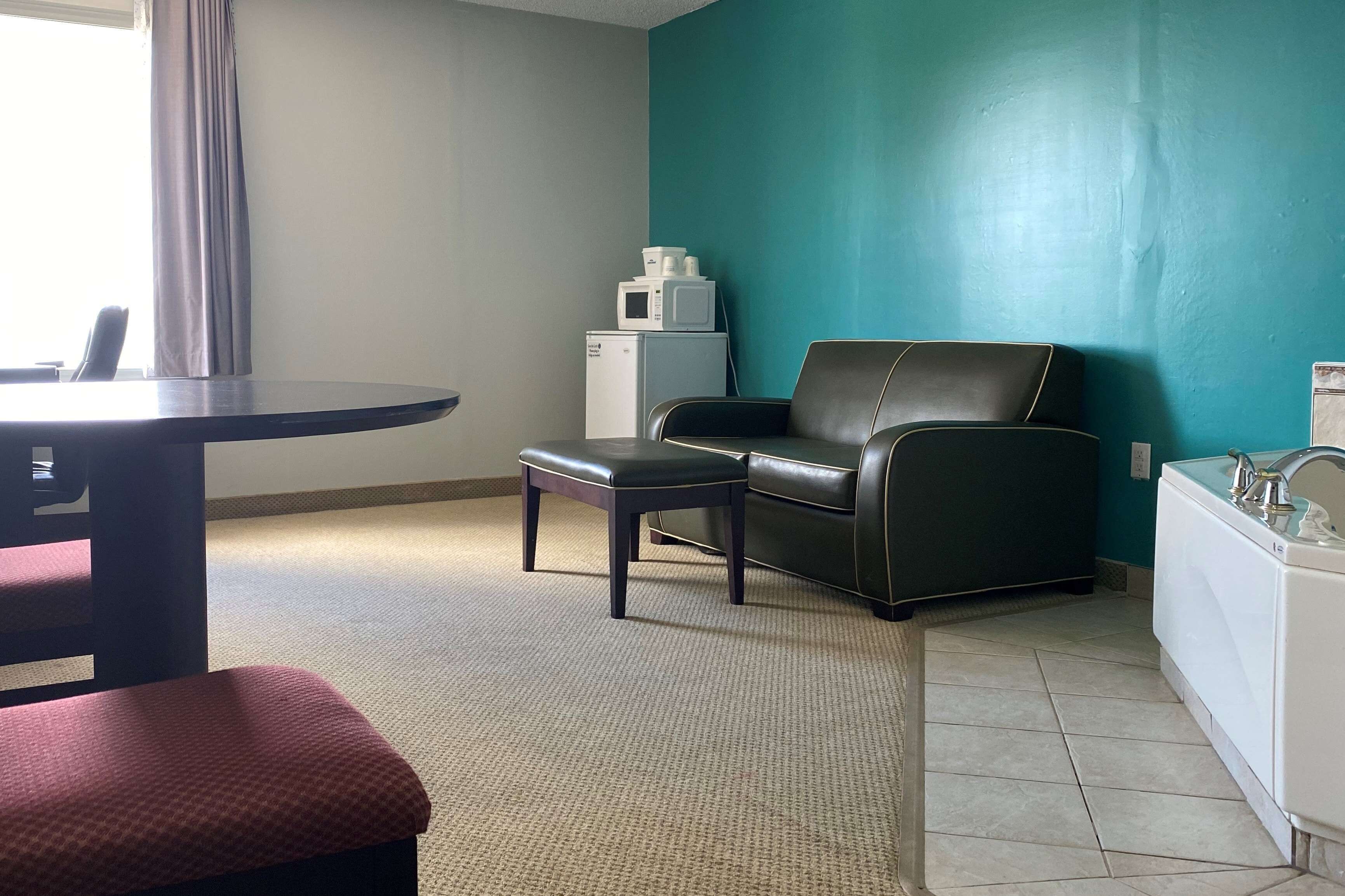 Une chambre d’hôtel avec un mur d’accent de couleur turquoise, un canapé en cuir noir, une petite table, un réfrigérateur blanc et un lavabo blanc.
