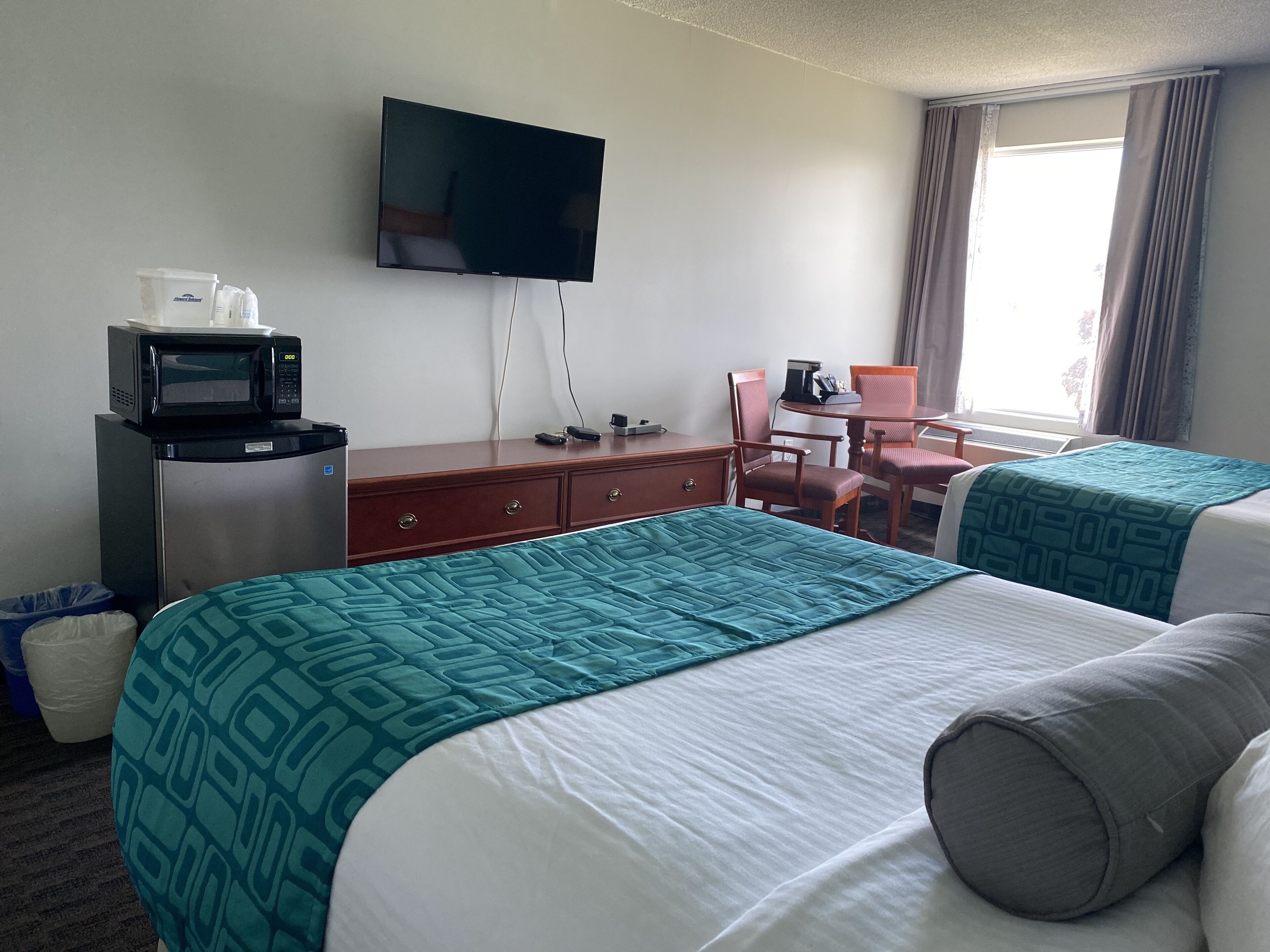 A hotel room with two beds, a desk with a chair, a television, a microwave, and a window with curtains.