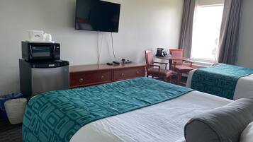 A hotel room with two beds, a desk with a chair, a television, a microwave, and a window with curtains.