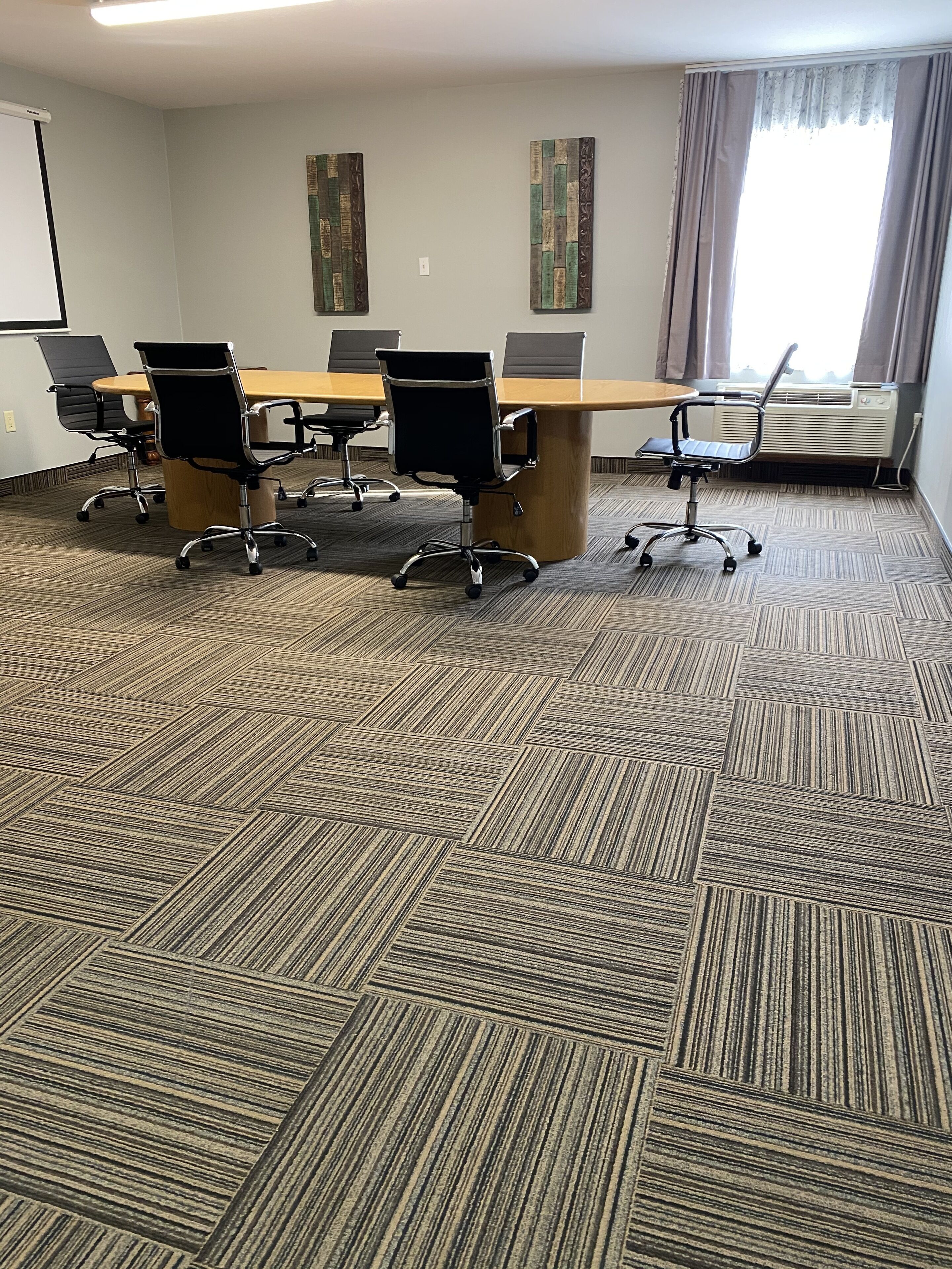 A conference room with a long table, six black office chairs, and two decorative wall pieces.