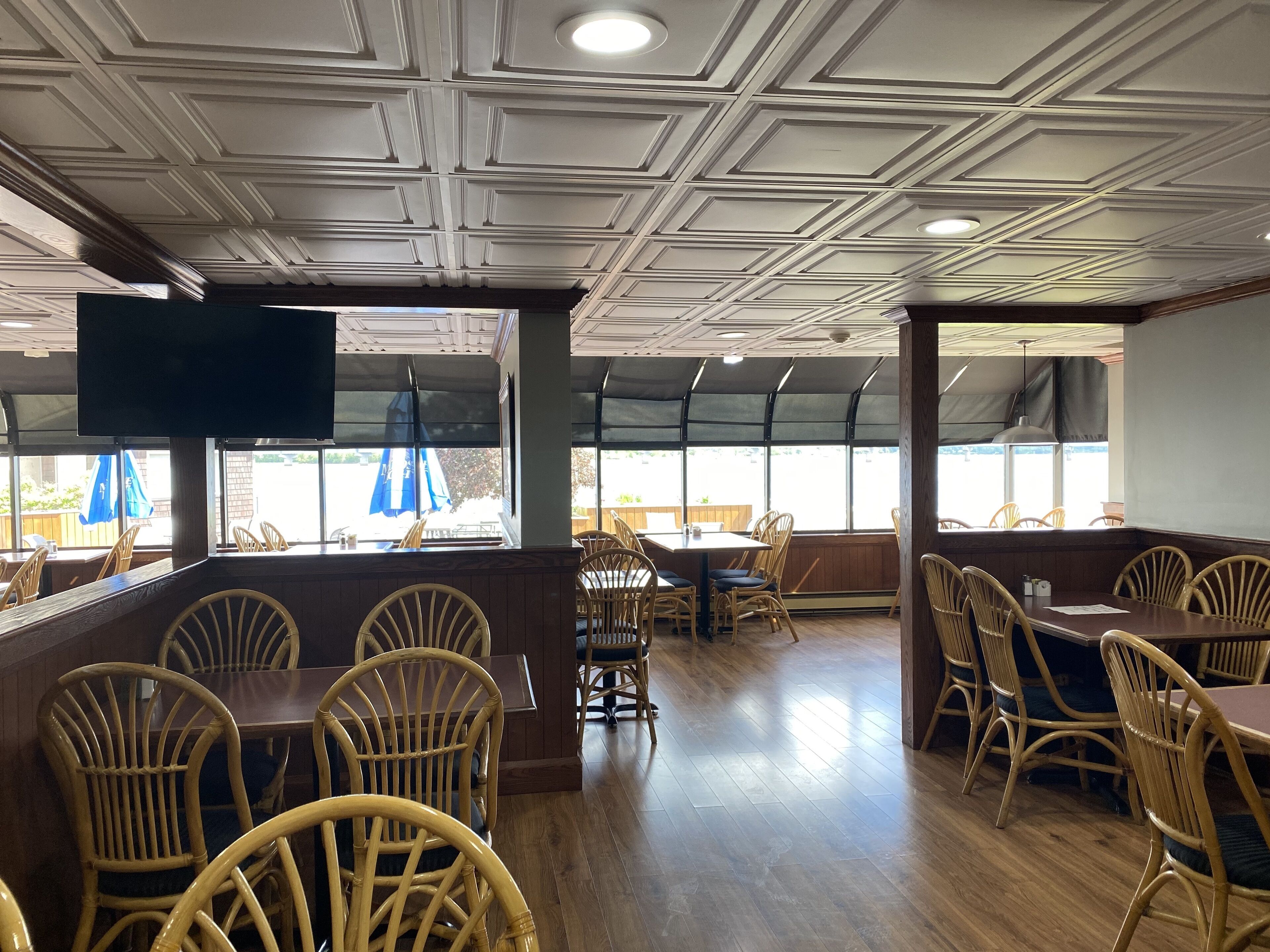 A restaurant interior with wooden flooring, wicker chairs, and tables.