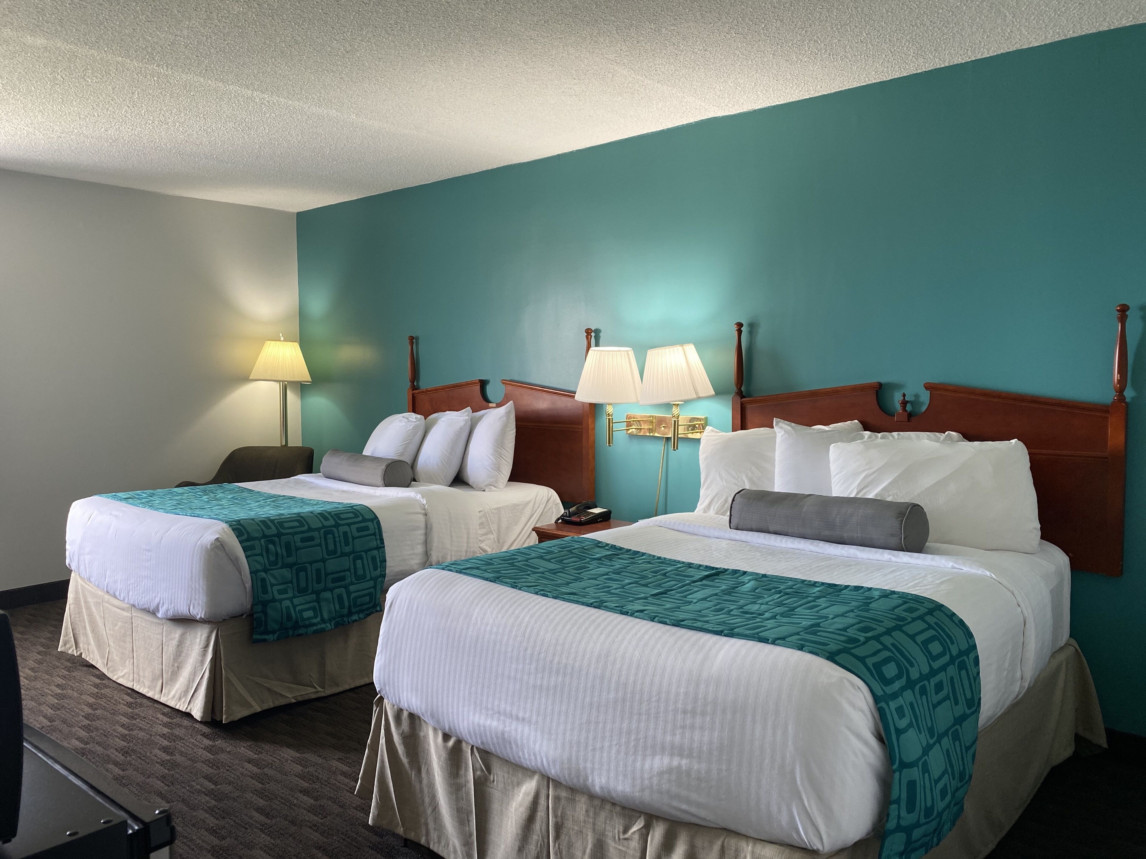 A hotel room with two beds, teal walls, and a wooden headboard.