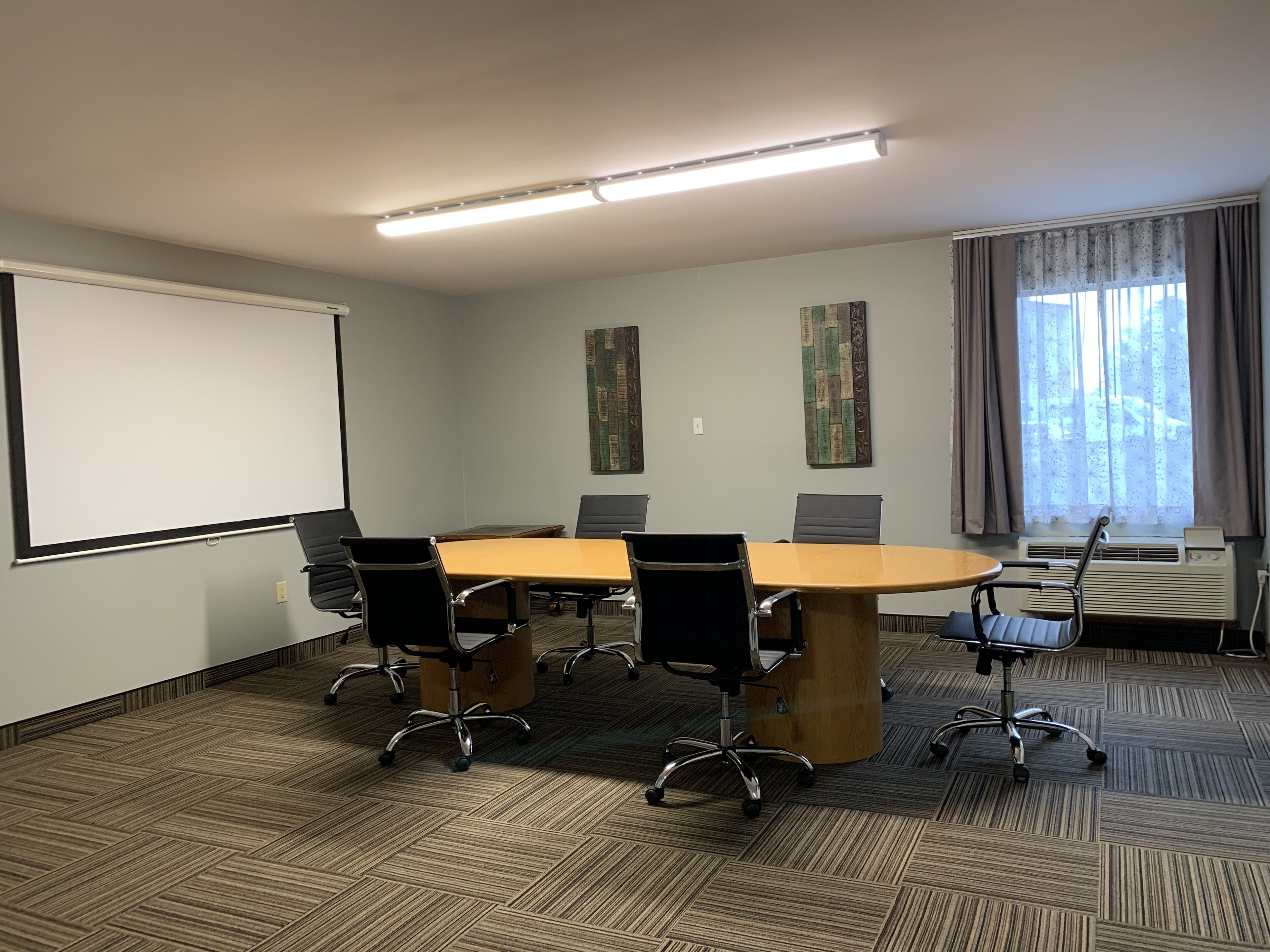 Een vergaderruimte met een grote tafel, vier stoelen, een scherm voor een projector en een raam met gordijnen.