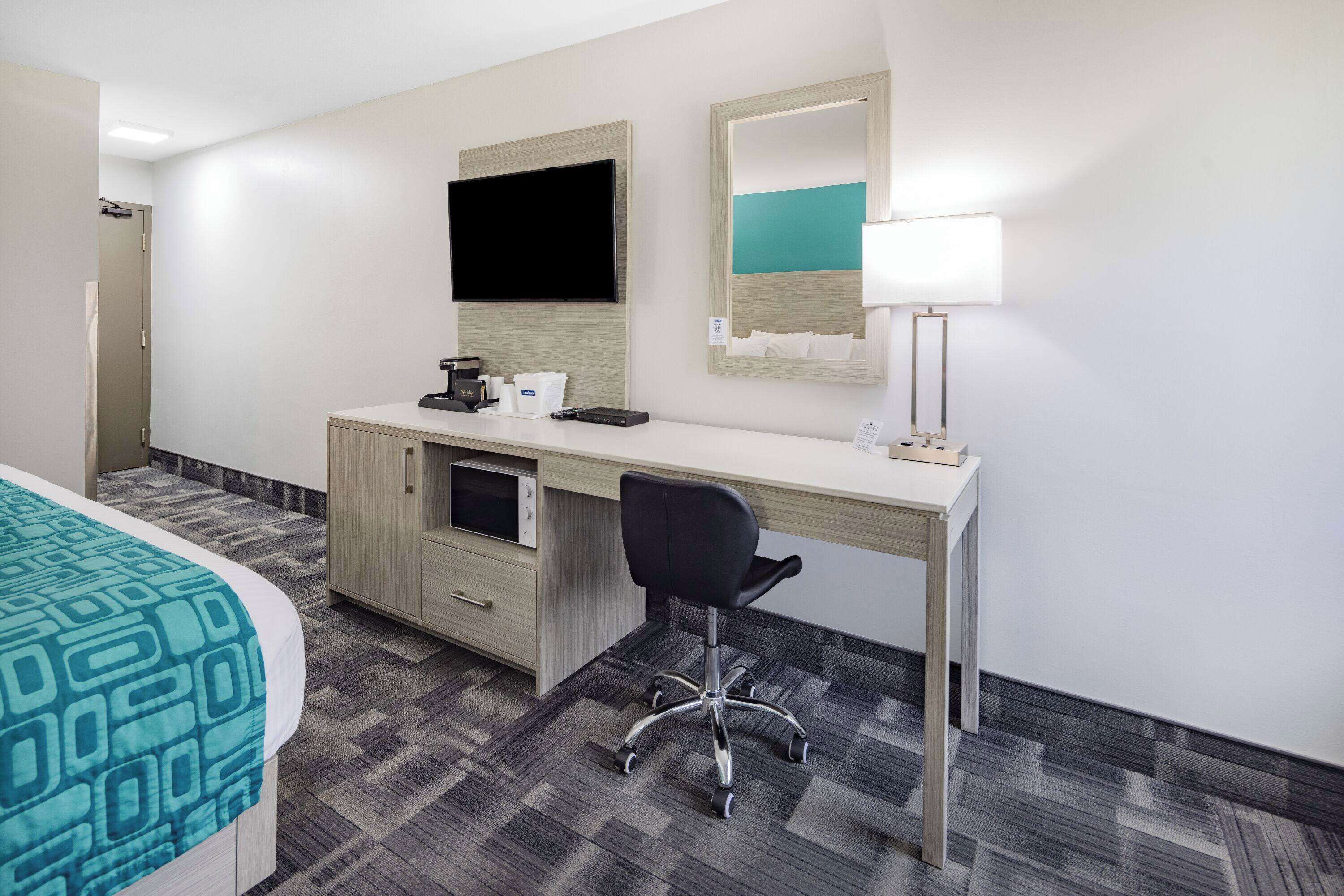 Une chambre d’hôtel comprenant un lit, un bureau avec un ordinateur, une chaise, une télévision et une lampe.