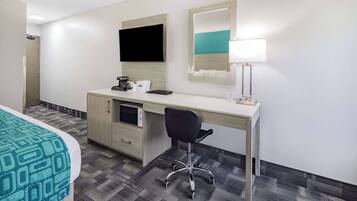 Une chambre d’hôtel comprenant un lit, un bureau avec un ordinateur, une chaise, une télévision et une lampe.