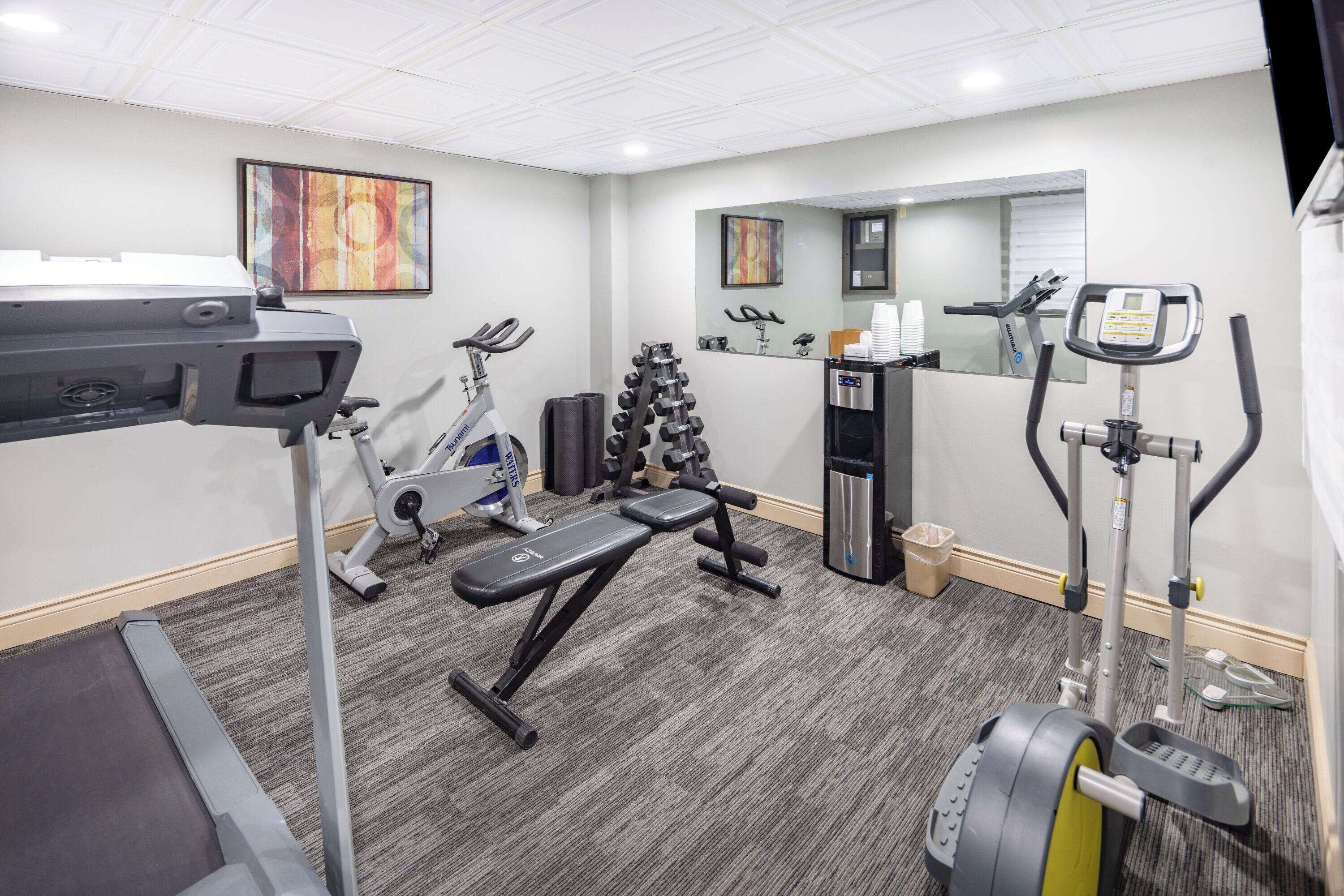Un gimnasio con equipo de ejercicio, una banca, mancuernas y una cinta de correr.