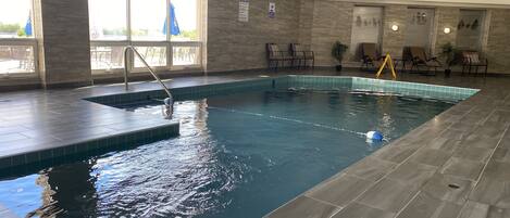 An indoor swimming pool with clear water, a diving board, and a lifeguard chair.