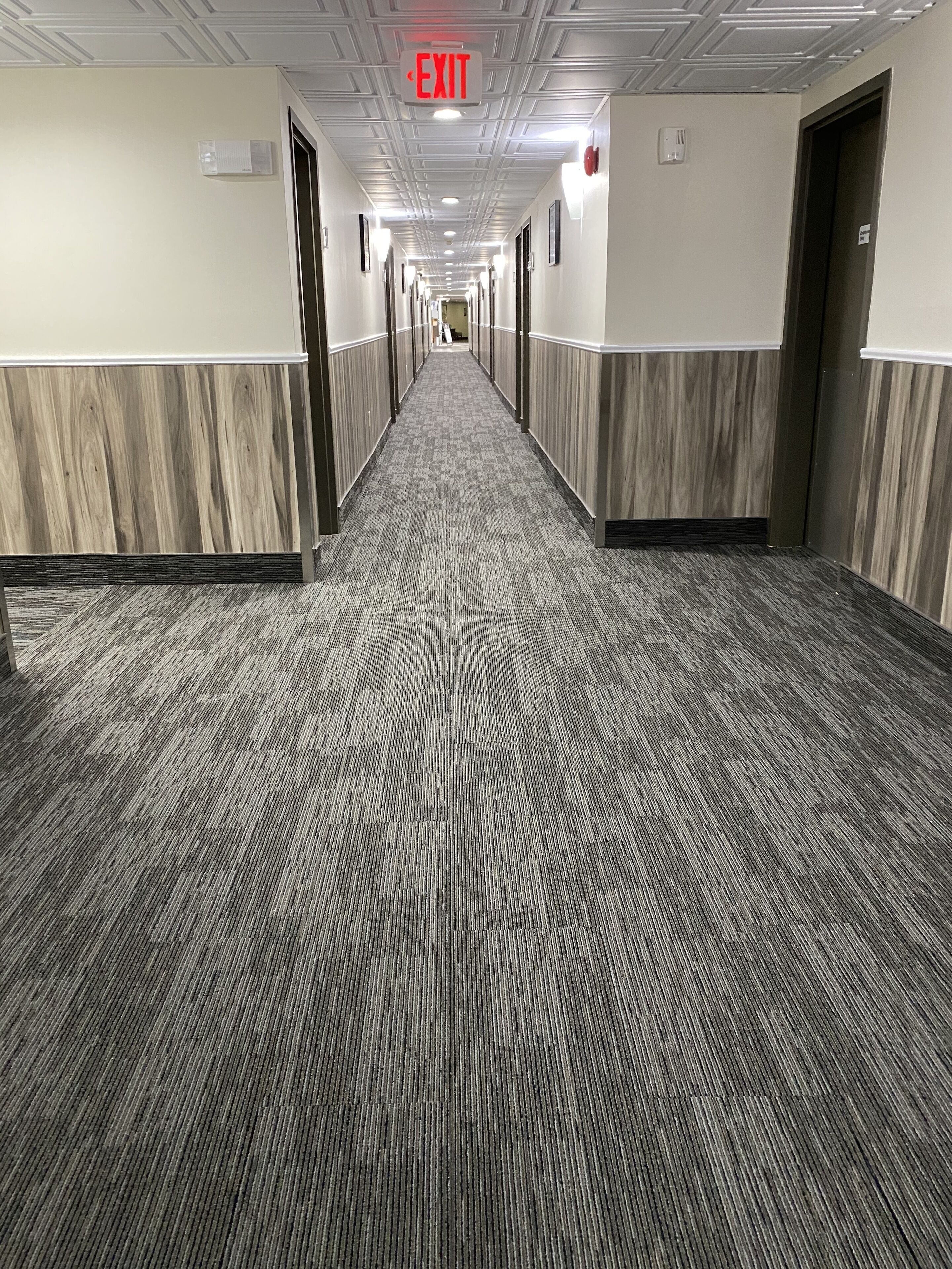 A hotel hallway with a patterned carpet, white walls, and doors on both sides.