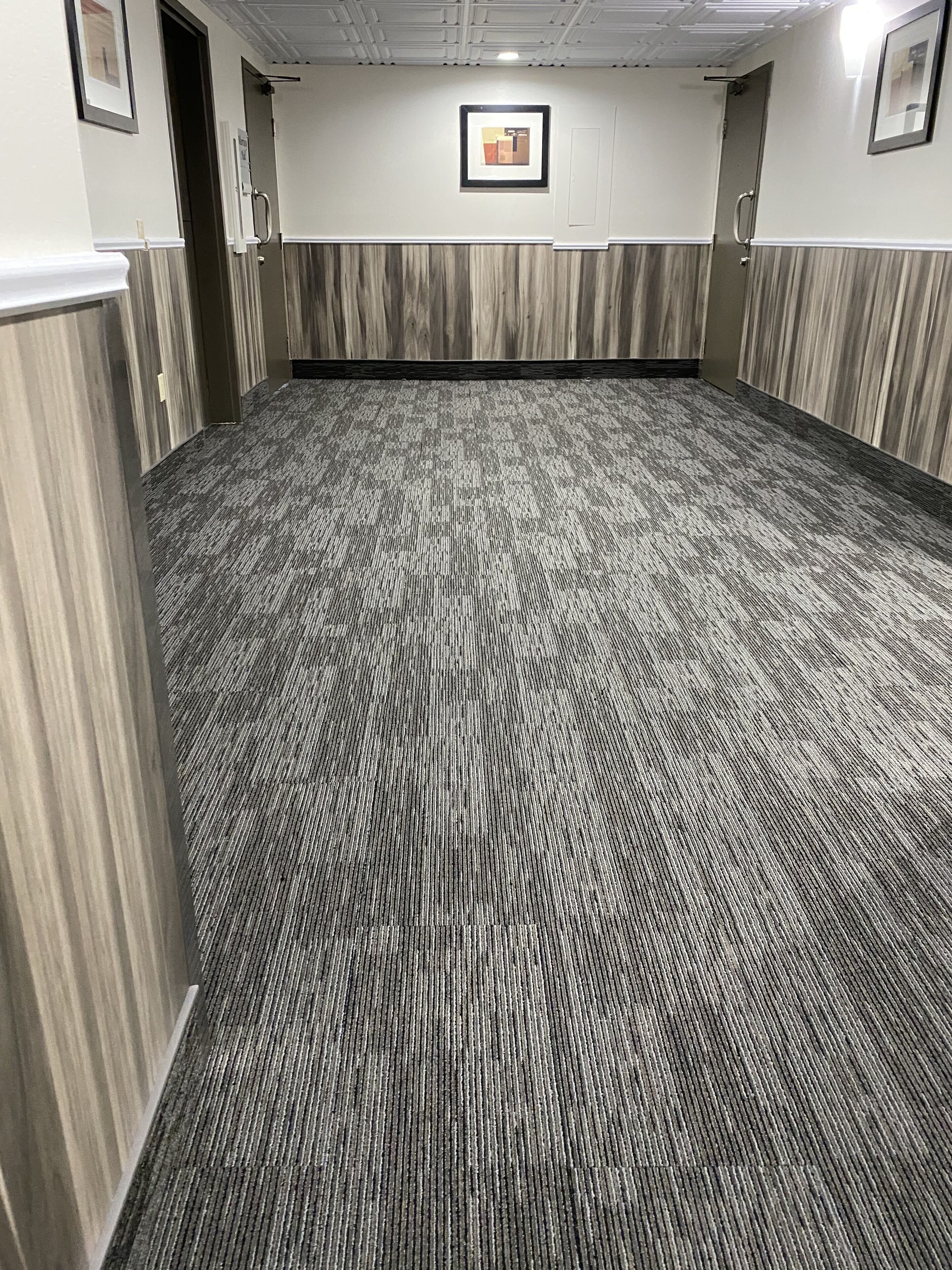 A carpeted hallway with a patterned floor, wooden paneling on the walls, and framed pictures on the walls.