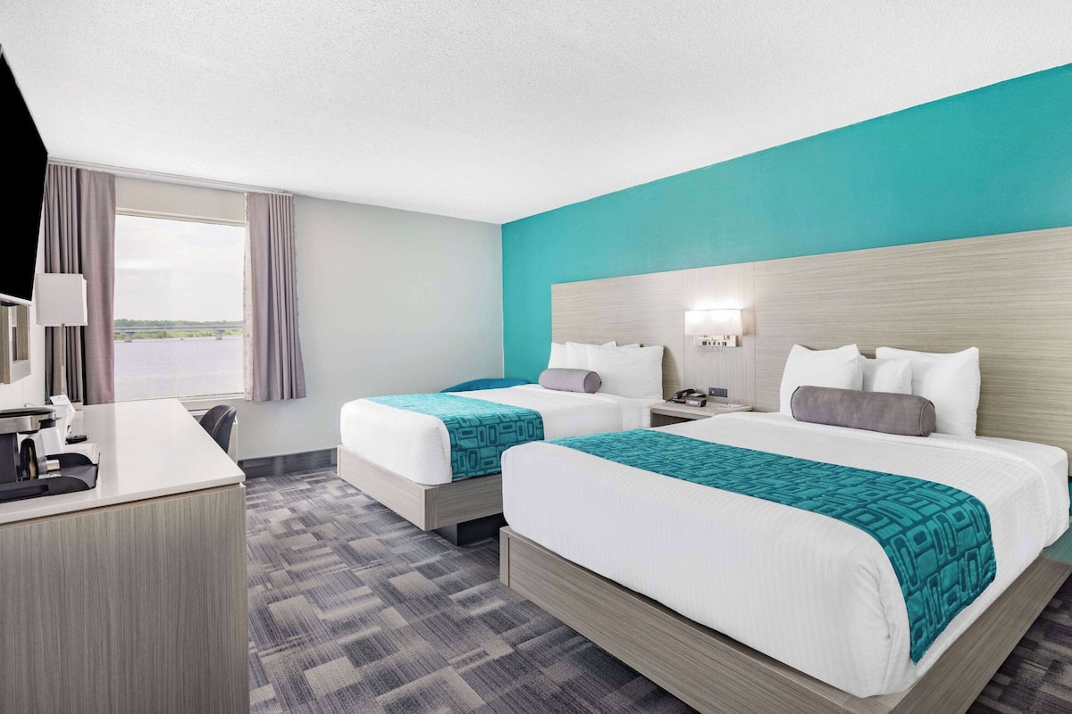 A hotel room with two beds, a desk, and a window with curtains.