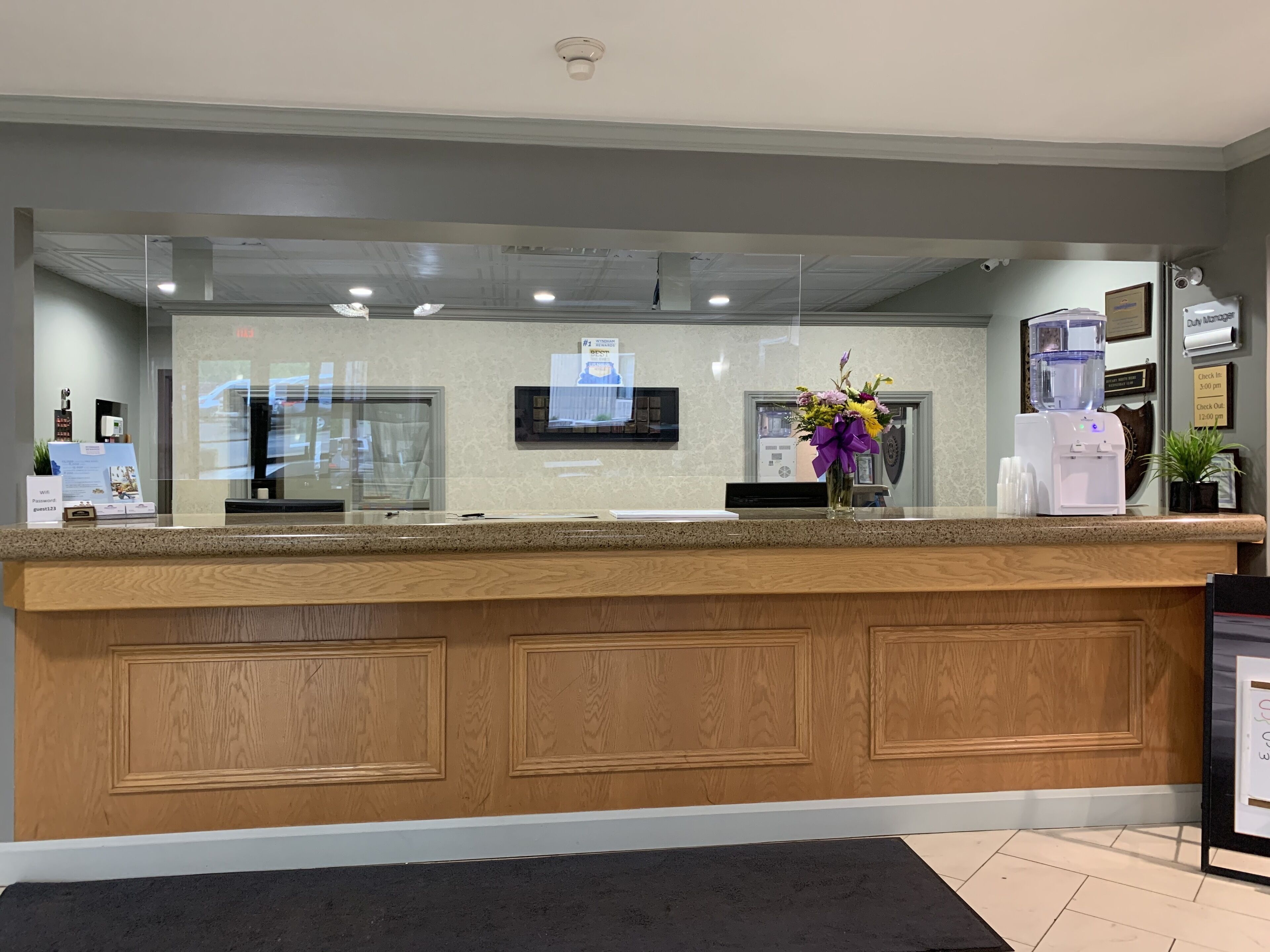 A reception desk with a wooden panel design, a glass partition, a water dispenser, and a framed welcome sign.