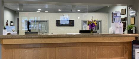 A reception desk with a wooden panel design, a glass partition, a water dispenser, and a framed welcome sign.