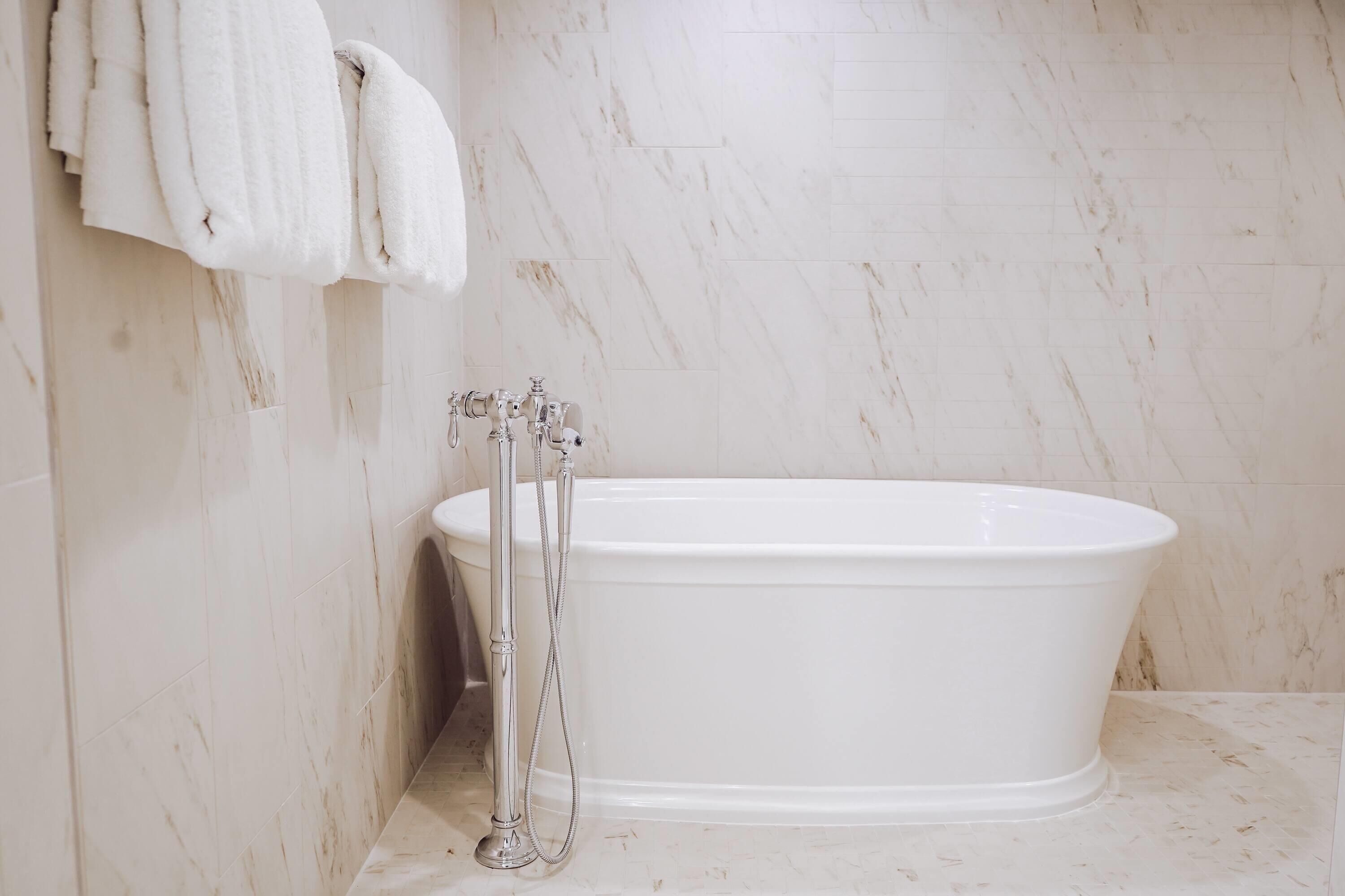 A bathroom with a white bathtub, a shower, and a marble wall.