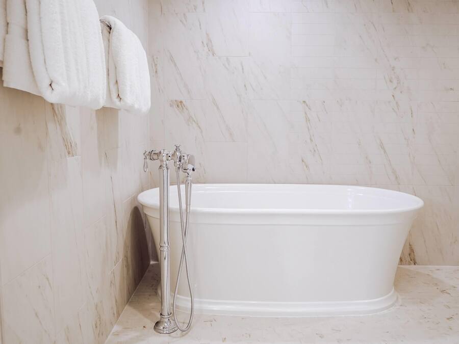 A bathroom with a white bathtub, a shower, and a marble wall.