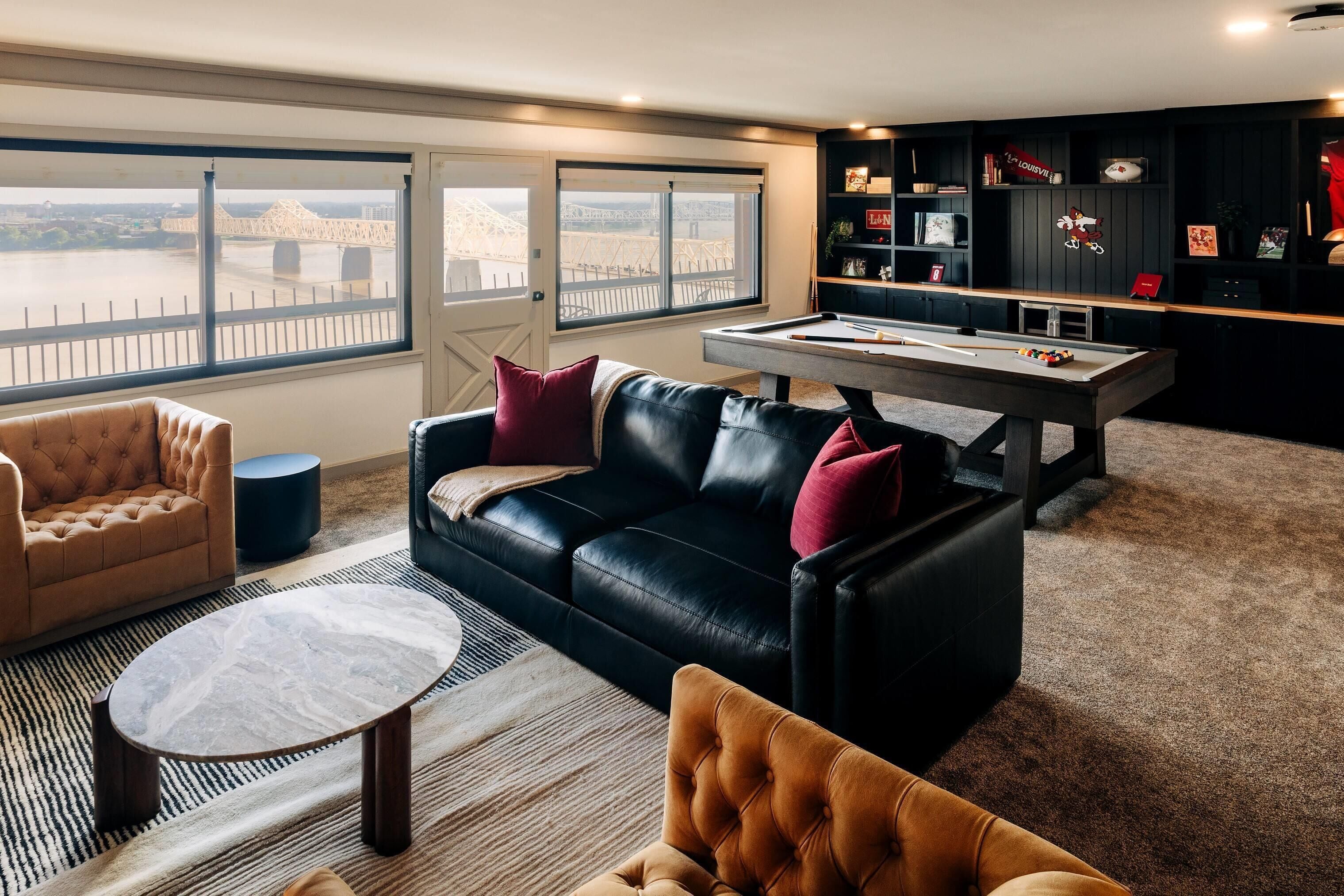 A living room with a pool table, leather sofas, and a view of a bridge.