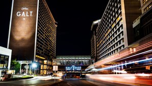 A nighttime view of The GALT and The Galthouse buildings with illuminated signage, a busy street with light trails from moving vehicles, and a modern urban setting.