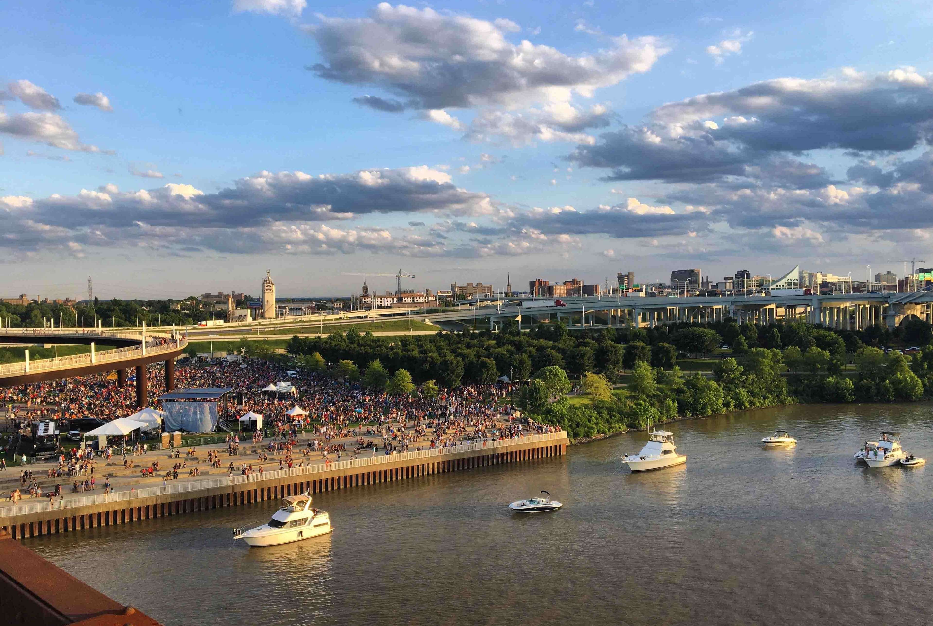 A riverside view with boats, a crowd, and a bridge.