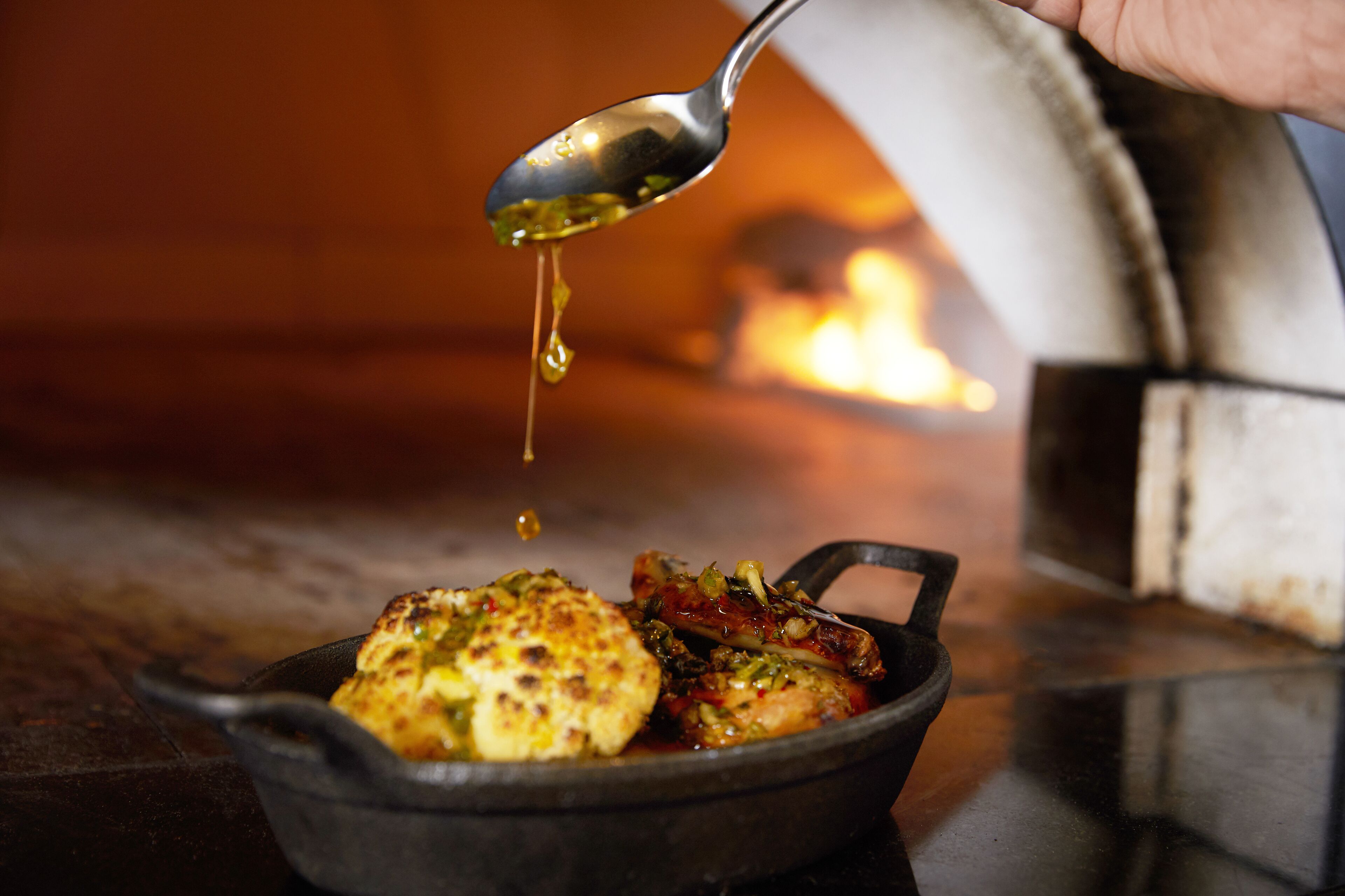A cast iron skillet with food being drizzled with sauce.