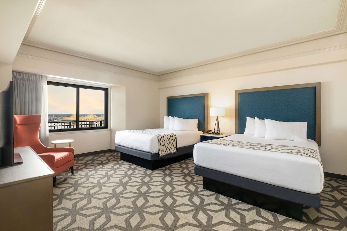 A hotel room with two beds, a desk, a chair, and a large window with a view.